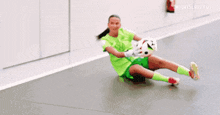 a female soccer player is kneeling on the floor holding a ball .