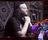 a man with a headband is sitting in front of a bookshelf and a cartoon character