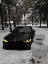 a black car is parked next to a snowman in the snow
