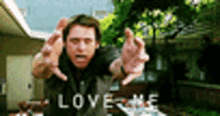 a man is standing in front of a house with his hands outstretched and the words love me written on the ground .