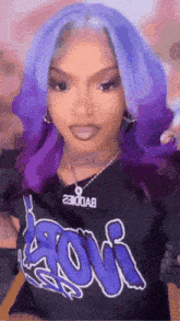 a woman with purple hair is wearing a black t-shirt with a necklace and earrings .