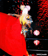 a woman in a colorful costume is dancing on a stage with a red cape behind her ..