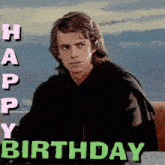 a man in a black jacket is sitting in front of a sign that says happy birthday .
