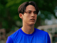 a young man wearing a blue shirt is looking at the camera