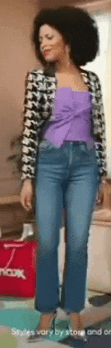 a woman wearing a purple top and blue jeans is standing in front of a red bag