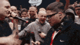 a man wearing a black nike jacket is singing into a microphone in front of a crowd