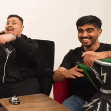 two men are sitting next to each other and one of them is wearing a black shirt with the letter g on it