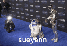 a man taking a picture of a r2d2 robot on a blue carpet with the name sueyann on it