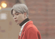 a man wearing a red jacket and a black turtleneck looks at the camera