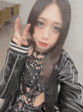 a woman wearing a black jacket and a choker is giving the peace sign