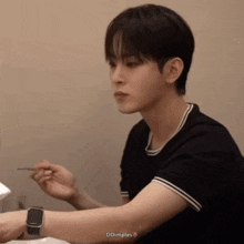 a young man wearing a watch is sitting at a table eating with chopsticks