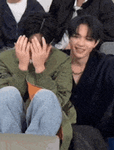 two young men are sitting next to each other covering their faces with their hands