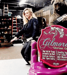 a woman is standing next to a purple gilmore sign