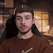 a man with a beard wearing a hat and a brown nike shirt