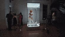 a woman in a white outfit is standing in a display case surrounded by people