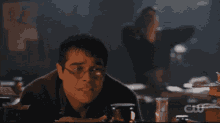 a man wearing glasses sits at a table with a cw logo in the corner