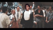 a man in a tuxedo is surrounded by a crowd of men