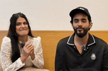 a man and a woman are sitting next to each other and the man is wearing a black hat that says " black "