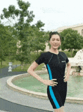 a woman wearing a black and blue swimsuit stands in front of a fountain