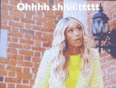 a woman in a yellow jacket is standing in front of a brick wall and says ohhhh shiiiittttt .
