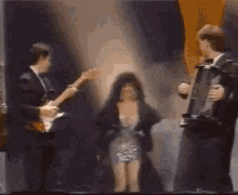 a woman in a dress is standing in front of two men playing instruments