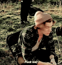 a man wearing a plaid shirt and a beanie is sitting in a chair and says fuck me .