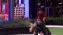 a woman in a red shirt is carrying a man on her back on a field .
