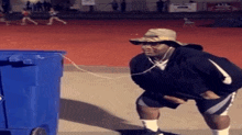 a man wearing headphones and a hat is standing next to a blue trash can