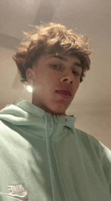 a young man with curly hair is wearing a light blue nike hoodie .