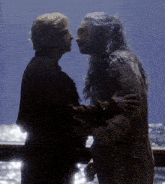 a man and a woman are looking at each other with the ocean in the background