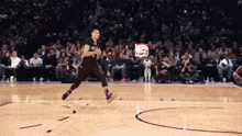 a basketball player is jumping in the air on a court with a crowd watching