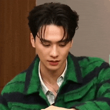 a young man wearing a green and black striped jacket and a white shirt is looking at the camera .