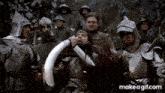 a group of men in armor are standing around a man in armor holding a horn in his mouth .
