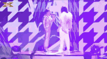 two people singing on a stage with a x on the bottom right