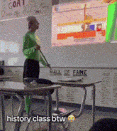 a man in a green shirt is standing in front of a white board that says hall of fame on it