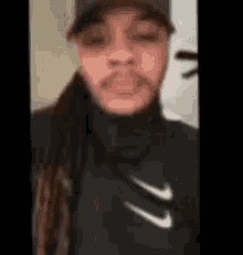 a man with dreadlocks is wearing a hat and a black nike jacket .