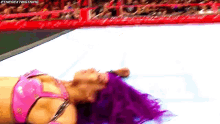 a woman with purple hair is laying on the ground in a wrestling ring .