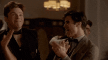 a man in a suit and bow tie applauds another man
