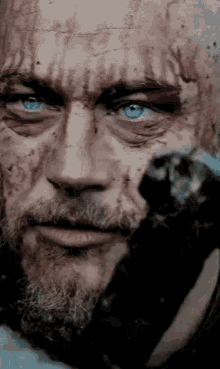 a man with a beard and blue eyes is covered in blood and has blood on his face .