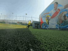 a man in a yellow shirt is running on a soccer field with a mural of a soccer player in the background