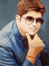 a young man wearing sunglasses and a leather jacket has his hand on his chin
