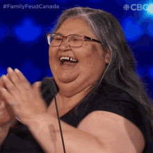 a woman wearing glasses is laughing and clapping in front of a microphone with the hashtag familyfeud canada