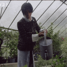 a man watering plants in a greenhouse with gue written on the bottom right
