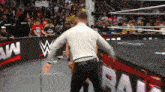 a man in a white shirt stands in a wrestling ring in front of a sign that says raw