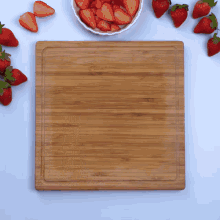 a wooden cutting board surrounded by strawberries on a table