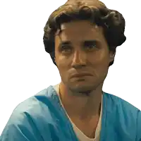 a man in a blue scrub top looks at the camera with a serious look on his face