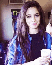 a girl holding a cup in front of a monster energy drink fridge