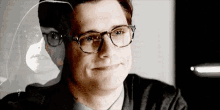 a man wearing glasses is smiling with a reflection of a woman in the glass .