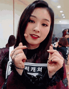 a woman making a heart shape with her hands while wearing a shirt with korean writing