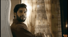 a man with a beard is sitting on a couch holding a cell phone .